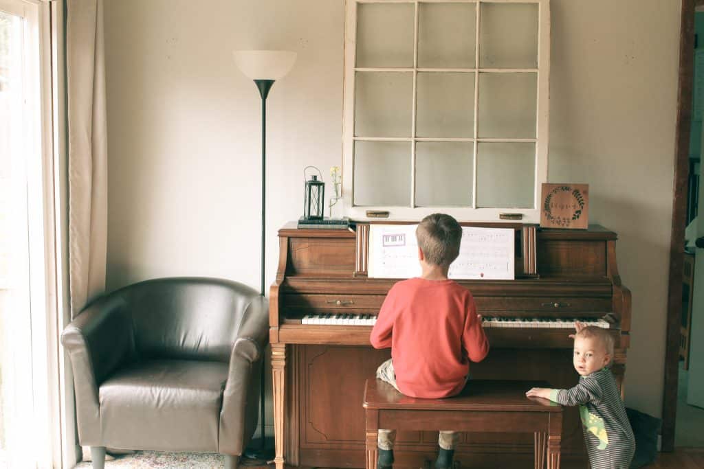 child practicing piano with baby brother at side