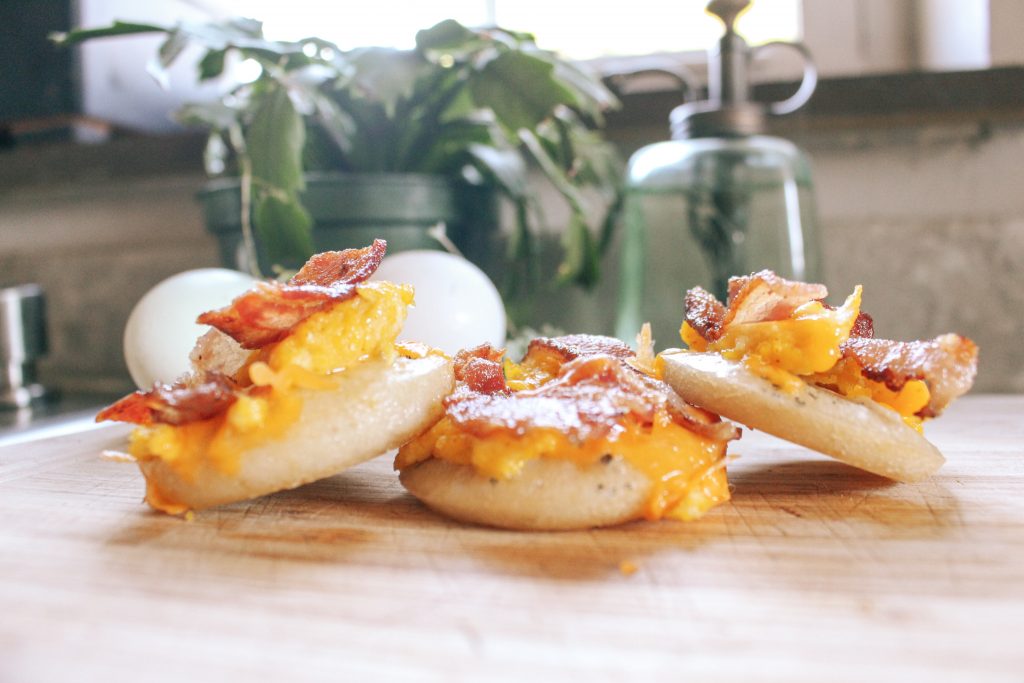 miniature sourdough breakfast pizzas with eggs bacon and cheese on wooden cutting board
