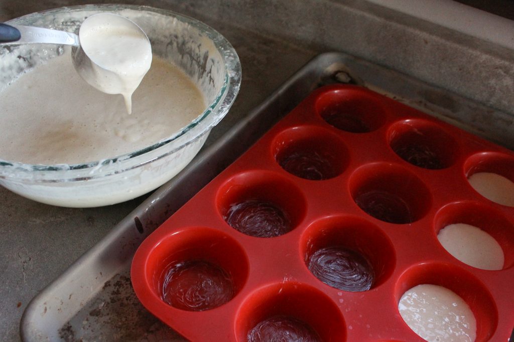 greased silicone muffin pan being filled with sourdough starter