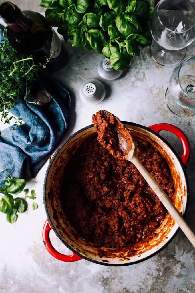 hearty meat sauce in dutch oven surrounded by fresh herbs