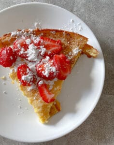 sliced sourdough dutch baby topped with strawberries and powdered sugar